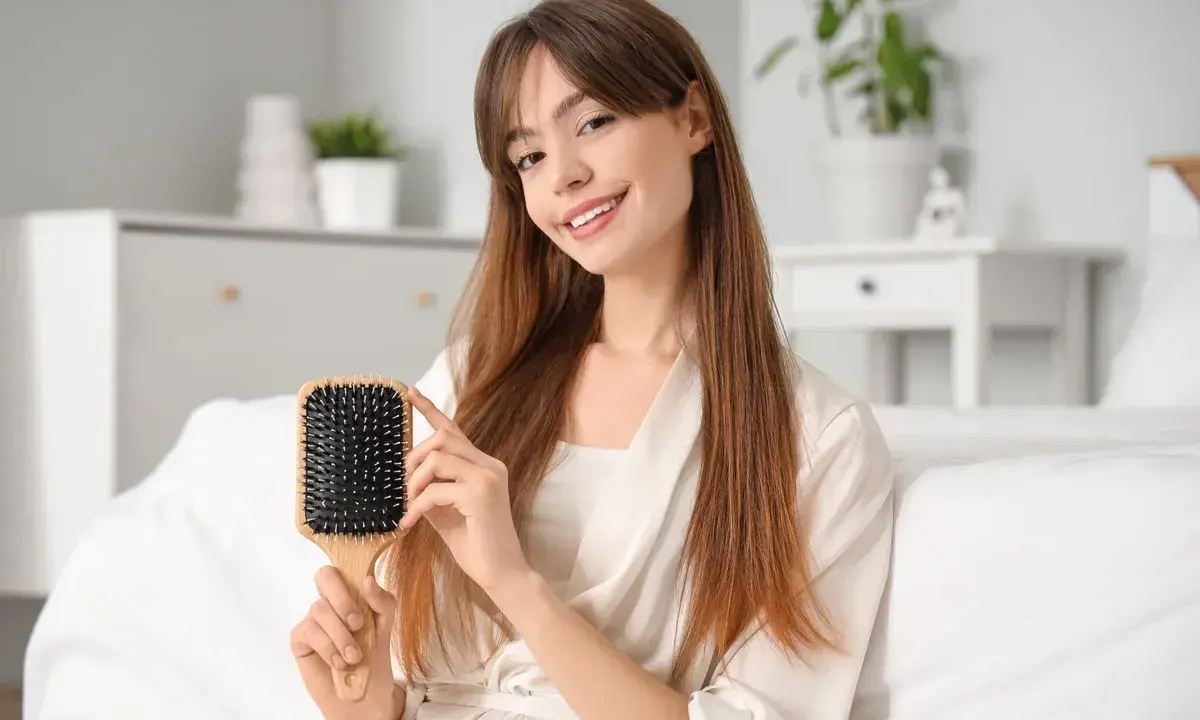 Ragazza sorridente mostra una spazzola per capelli in plastica, perfetta per districare e pulire i capelli.