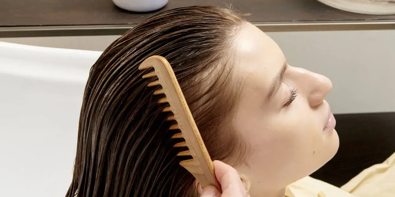 Una mano pettina delicatamente i capelli bagnati, sciogliendo eventuali nodi ai capelli dietro la nuca per una chioma fluente.