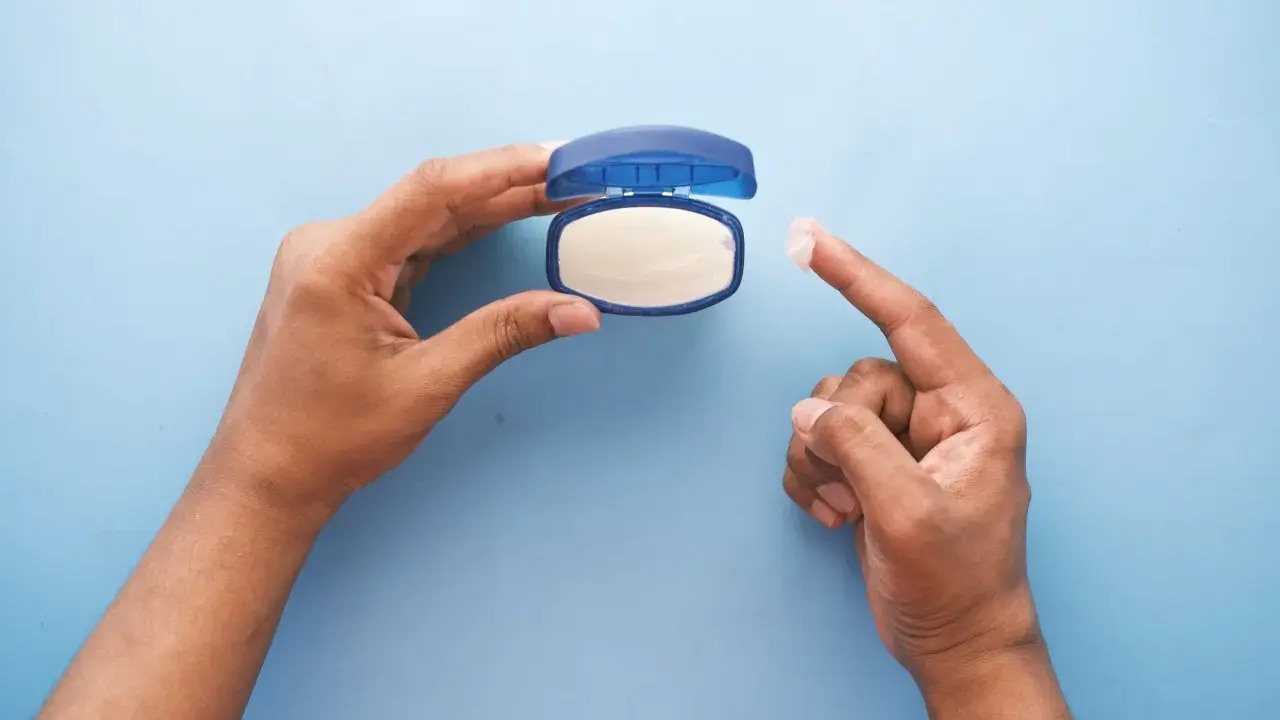 Mano che preleva vaselina per lenire l'irritazione da retinolo.