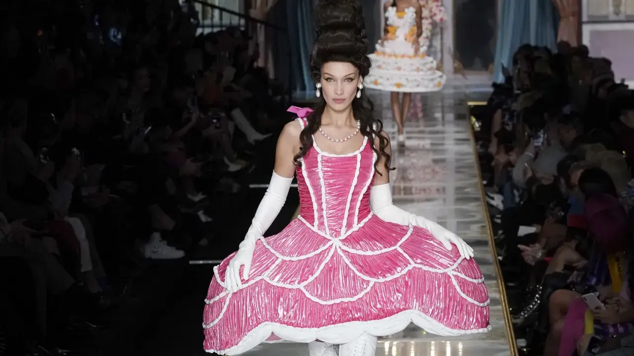 Modella con abito rosa Moschino abbigliamento donna, ispirato a una torta, con acconciatura voluminosa e guanti bianchi.