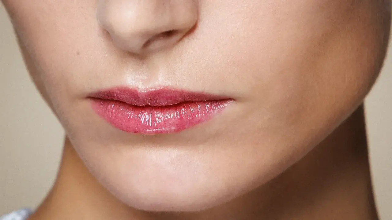 Labbra sottili valorizzate da un lucidalabbra rosa brillante, un trucco che dona volume e un aspetto pieno.