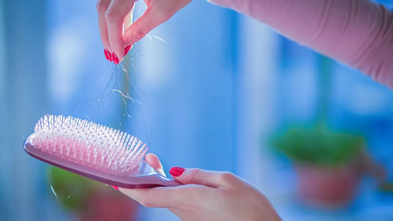 Mani con smalto rosso rimuovono capelli da una spazzola rosa. Un promemoria per imparare come lavare le spazzole per mantenerle pulite.