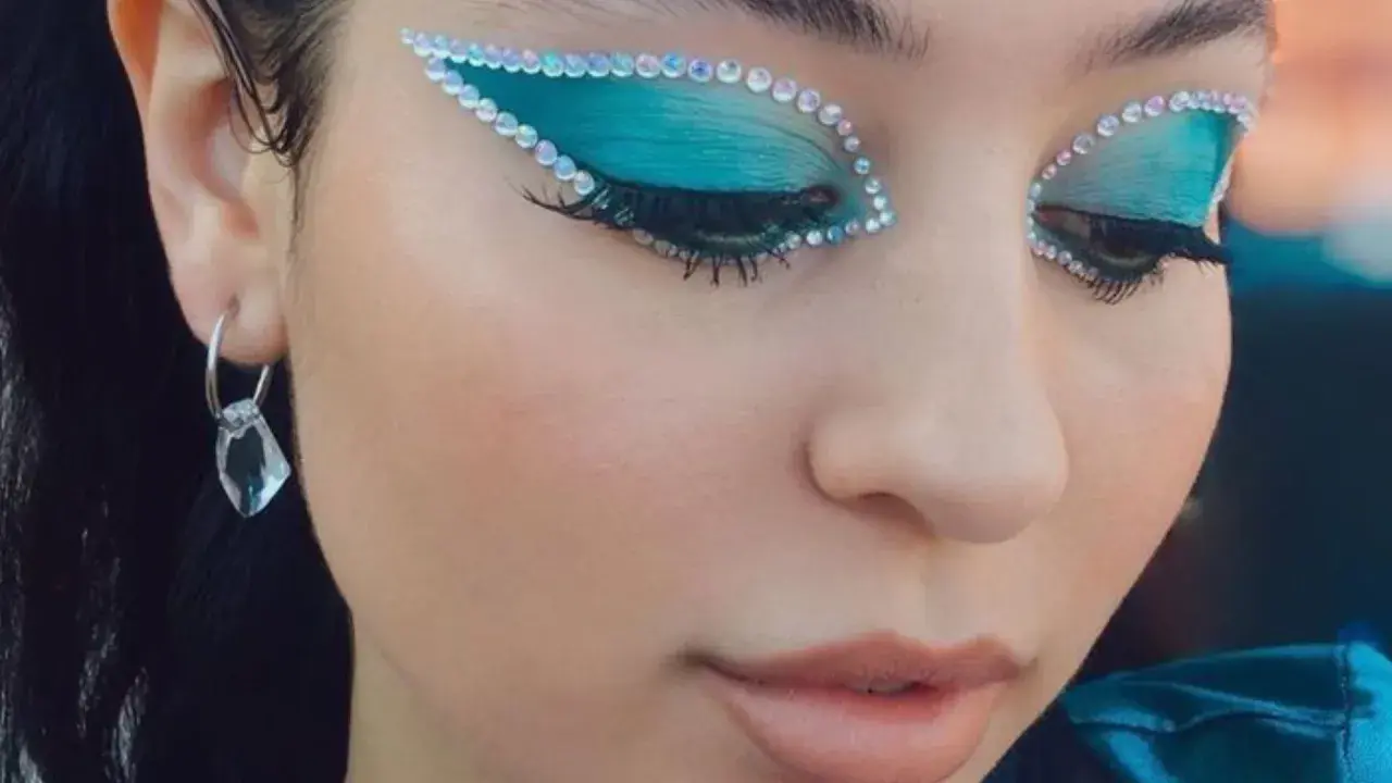 Occhi con ombretto blu elettrico e strass scintillanti, un look che fa make up euphoria. Orecchino pendente con cristallo.