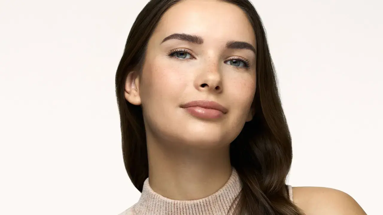 Primo piano di una giovane donna con lentiggini, labbra lucide e sopracciglia definite. Un look naturale, perfetto come trucco da fare per ogni occasione.