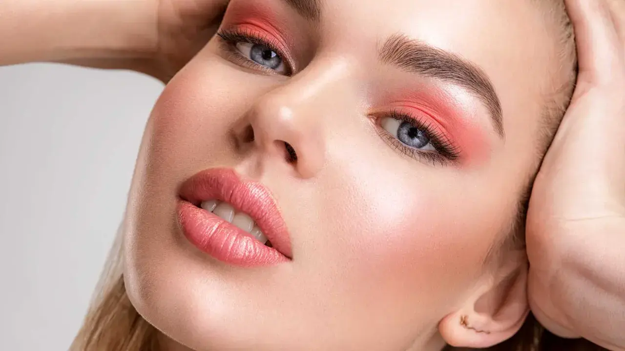 Viso di donna con trucco pesca: ombretto vivace, labbra lucide e un tocco di fard dove si mette il fard per un effetto radioso.