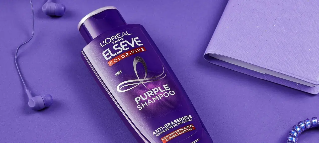 Flacone di shampoo viola L'Oréal Elseve Color-Vive, con auricolari e quaderno viola. Lo shampoo antigiallo schiarisce i capelli, neutralizzando i toni indesiderati.