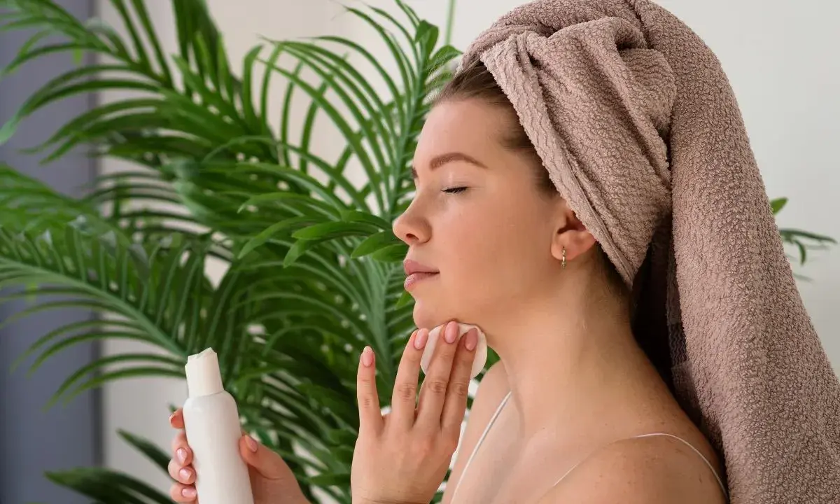 Donna con asciugamano in testa applica tonico sul viso con un dischetto di cotone, parte della sua **night skincare routine**.