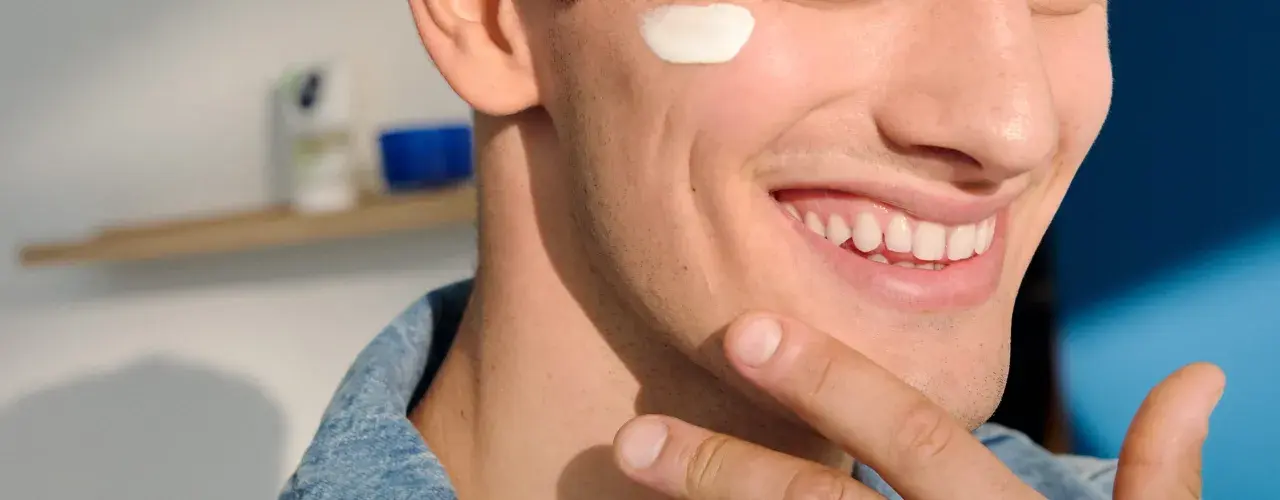 Uomo sorridente applica crema sul viso, forse per lenire l'irritazione da lametta quanto dura.