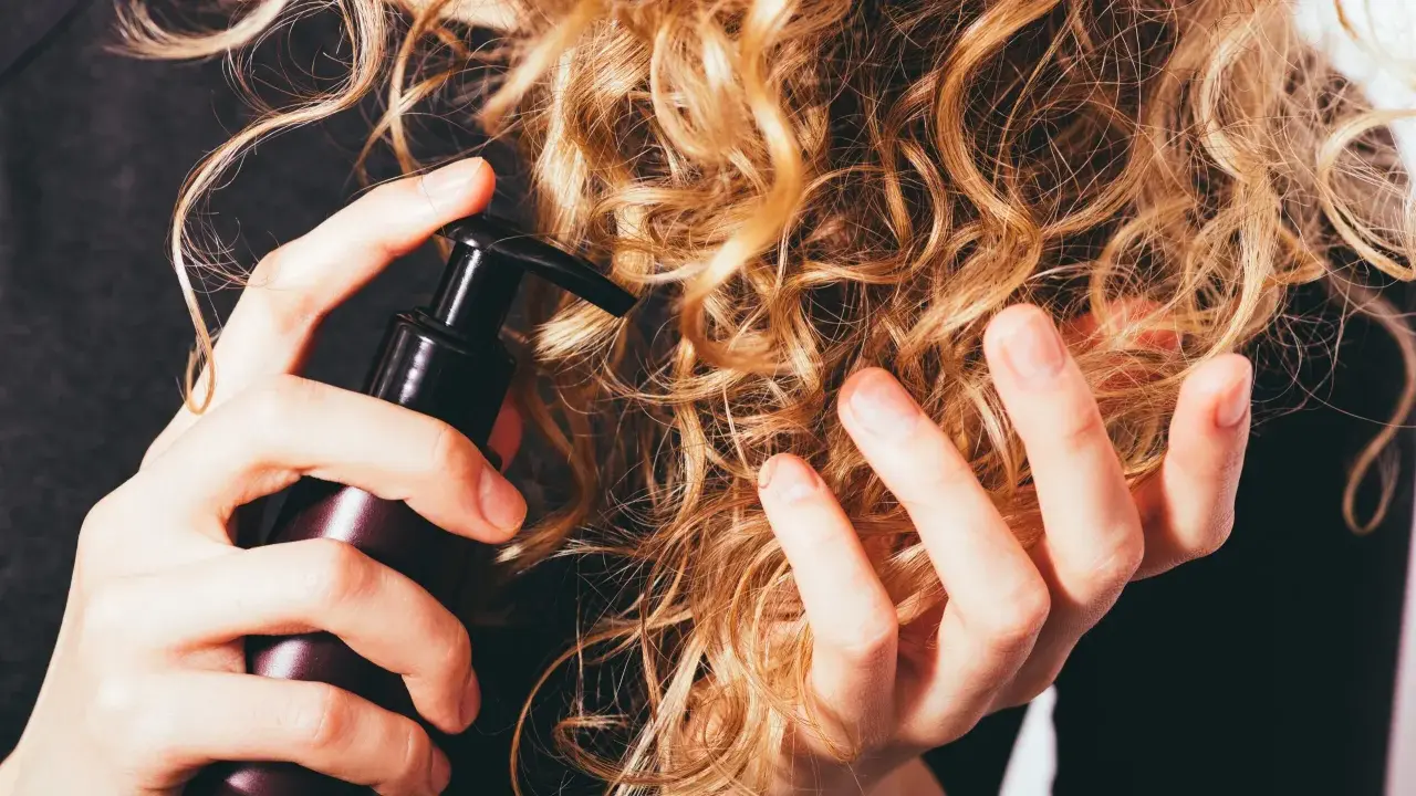 Mani che applicano un prodotto su capelli ricci secchi, per nutrirli e renderli morbidi.