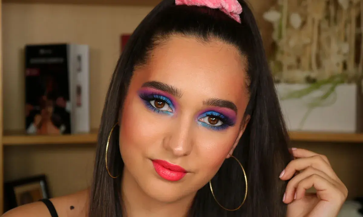 Ragazza con trucco occhi vivace blu e viola, labbra fucsia e scrunchie rosa. Un look ispirato al tutorial trucco anni 80.
