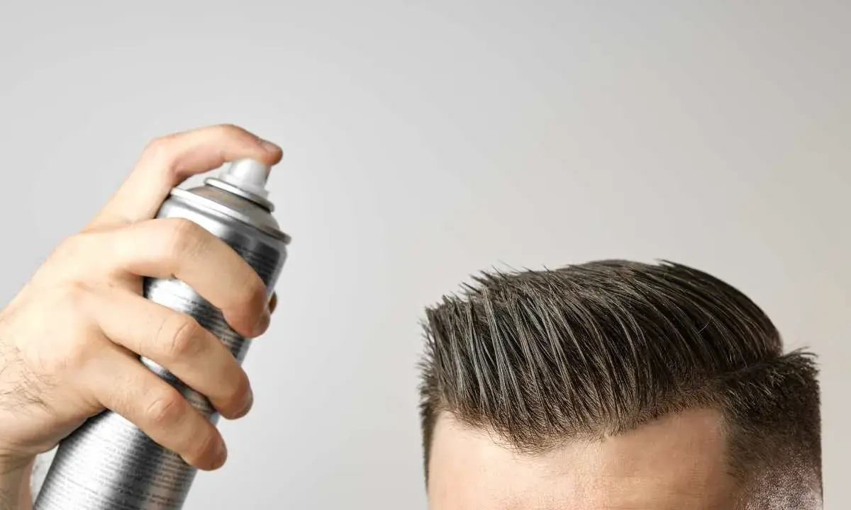 Mano che spruzza lacca sui capelli. Attenzione, la cera fa cadere i capelli, ma questo prodotto è per fissare.