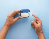Mano che preleva vaselina per lenire l'irritazione da retinolo.