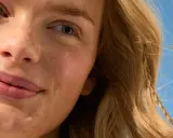 Viso sorridente con lentiggini, capelli biondi mossi dal vento. La sua pelle è protetta, una protezione 50 che dura 50 minuti sotto il sole.