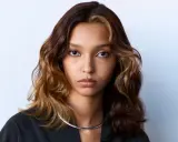 Volto di donna con capelli mossi castani e ciocche bionde, effetto colore demipermanente. Indossa una collana argentata.