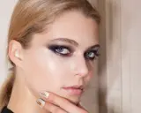 Ragazza con trucco appariscente sugli occhi, labbra naturali e unghie bianche con dettagli oro.