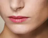 Labbra sottili valorizzate da un lucidalabbra rosa brillante, un trucco che dona volume e un aspetto pieno.