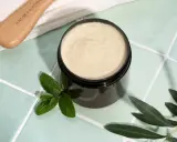 Vaso di scrub cuoio capelluto fai da te con menta e foglie d'ulivo. Un pettine in legno è visibile in alto a sinistra.