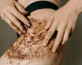 Mani che applicano uno scrub corpo al caffè sulla pelle. Un gesto per scoprire come fare lo scrub corpo e ottenere una pelle liscia e luminosa.