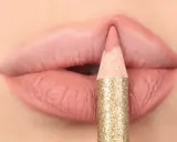 Matita glitterata color oro definisce il contorno delle labbra con un tratto preciso, creando un effetto overline labbra impeccabile.