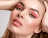 Viso di donna con trucco pesca: ombretto vivace, labbra lucide e un tocco di fard dove si mette il fard per un effetto radioso.