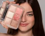 Una donna sorride mostrando una palette di make up elegante con sei cialde di diverse tonalità rosate e luminose.