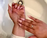 Mani con scrub per capire come togliere l'autoabbronzante. Unghie rosa e anello con cuore.