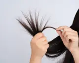 Mani che esaminano ciocche di capelli scuri, mostrando le doppie punte come causa di capelli danneggiati e secchi.