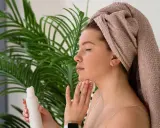 Donna con asciugamano in testa applica tonico sul viso con un dischetto di cotone, parte della sua **night skincare routine**.