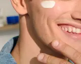 Uomo sorridente applica crema sul viso, forse per lenire l'irritazione da lametta quanto dura.