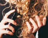 Mani che applicano un prodotto su capelli ricci secchi, per nutrirli e renderli morbidi.