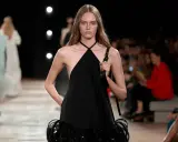 Modella con un abito nero legato al collo, con dettagli di piume sulla gonna, sfila in passerella.