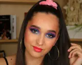 Ragazza con trucco occhi vivace blu e viola, labbra fucsia e scrunchie rosa. Un look ispirato al tutorial trucco anni 80.