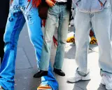 Gambe in primo piano con diversi modelli di moschino jeans: uno blu con inserti e ricami, uno più chiaro e sbiadito, e uno grigio chiaro oversize.