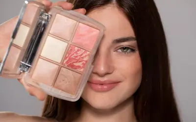 Una donna sorride mostrando una palette di make up elegante con sei cialde di diverse tonalità rosate e luminose.
