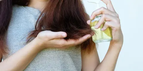 Donna applica olio di jojoba sui capelli, sfruttando le sue proprietà nutrienti per una chioma sana e lucente.