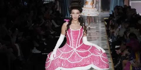 Modella con abito rosa Moschino abbigliamento donna, ispirato a una torta, con acconciatura voluminosa e guanti bianchi.