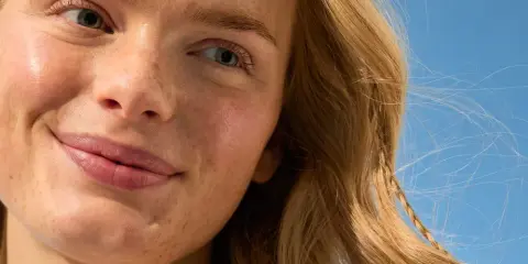 Viso sorridente con lentiggini, capelli biondi mossi dal vento. La sua pelle è protetta, una protezione 50 che dura 50 minuti sotto il sole.