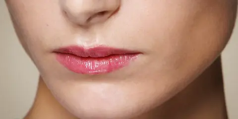 Labbra sottili valorizzate da un lucidalabbra rosa brillante, un trucco che dona volume e un aspetto pieno.