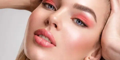 Viso di donna con trucco pesca: ombretto vivace, labbra lucide e un tocco di fard dove si mette il fard per un effetto radioso.