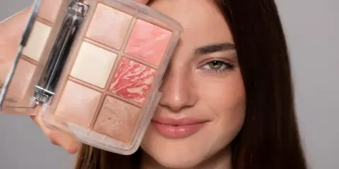 Una donna sorride mostrando una palette di make up elegante con sei cialde di diverse tonalità rosate e luminose.
