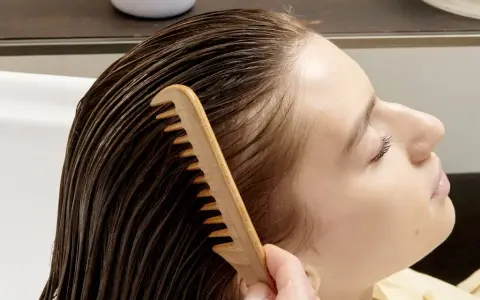 Una mano pettina delicatamente i capelli bagnati, sciogliendo eventuali nodi ai capelli dietro la nuca per una chioma fluente.