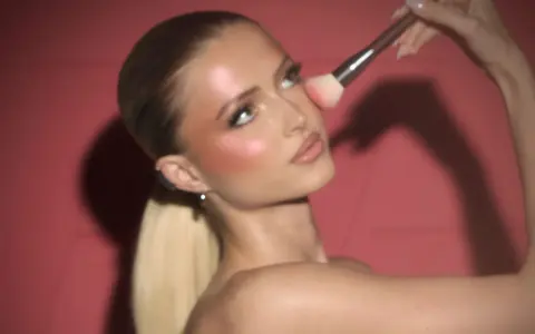 Donna bionda con un pennello applica il blush in polvere sulle guance per un look radioso.