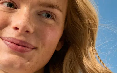 Viso sorridente con lentiggini, capelli biondi mossi dal vento. La sua pelle è protetta, una protezione 50 che dura 50 minuti sotto il sole.