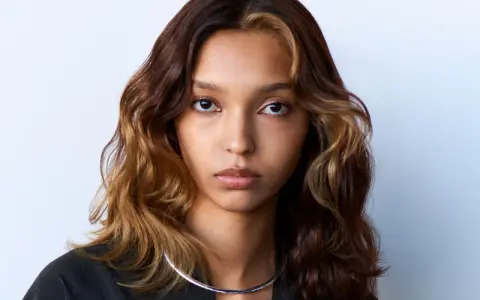 Volto di donna con capelli mossi castani e ciocche bionde, effetto colore demipermanente. Indossa una collana argentata.