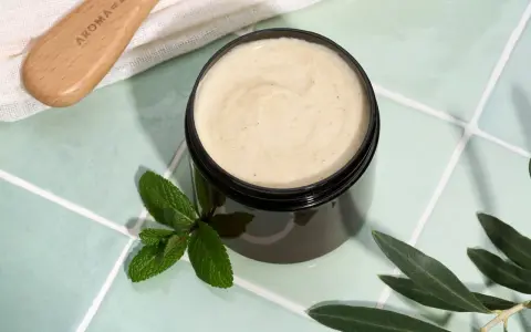 Vaso di scrub cuoio capelluto fai da te con menta e foglie d'ulivo. Un pettine in legno è visibile in alto a sinistra.