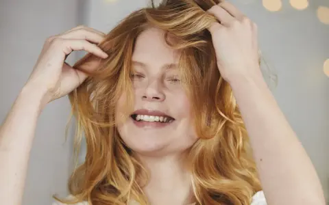 Ragazza con capelli rossi mossi che si sistema la chioma, un gesto per dare volume ai capelli.