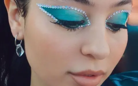 Occhi con ombretto blu elettrico e strass scintillanti, un look che fa make up euphoria. Orecchino pendente con cristallo.