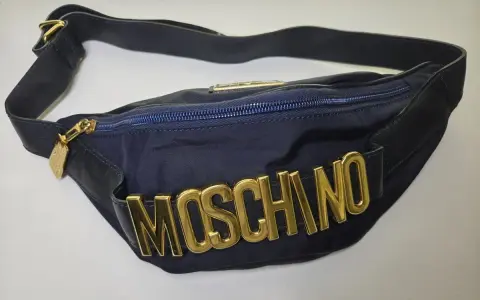 Borsa blu Moschino con logo dorato in rilievo, tracolla regolabile e zip. Un accessorio iconico per un look audace.