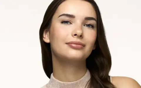Primo piano di una giovane donna con lentiggini, labbra lucide e sopracciglia definite. Un look naturale, perfetto come trucco da fare per ogni occasione.
