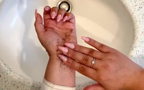Mani con scrub per capire come togliere l'autoabbronzante. Unghie rosa e anello con cuore.